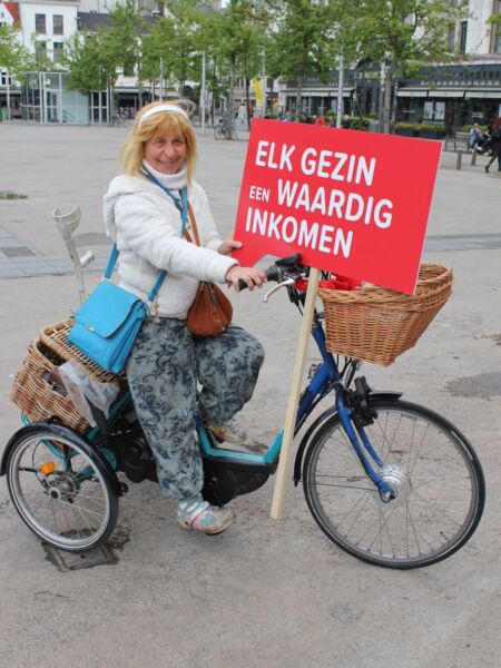 Mevrouw op fiets met bord Komafmetarmoede